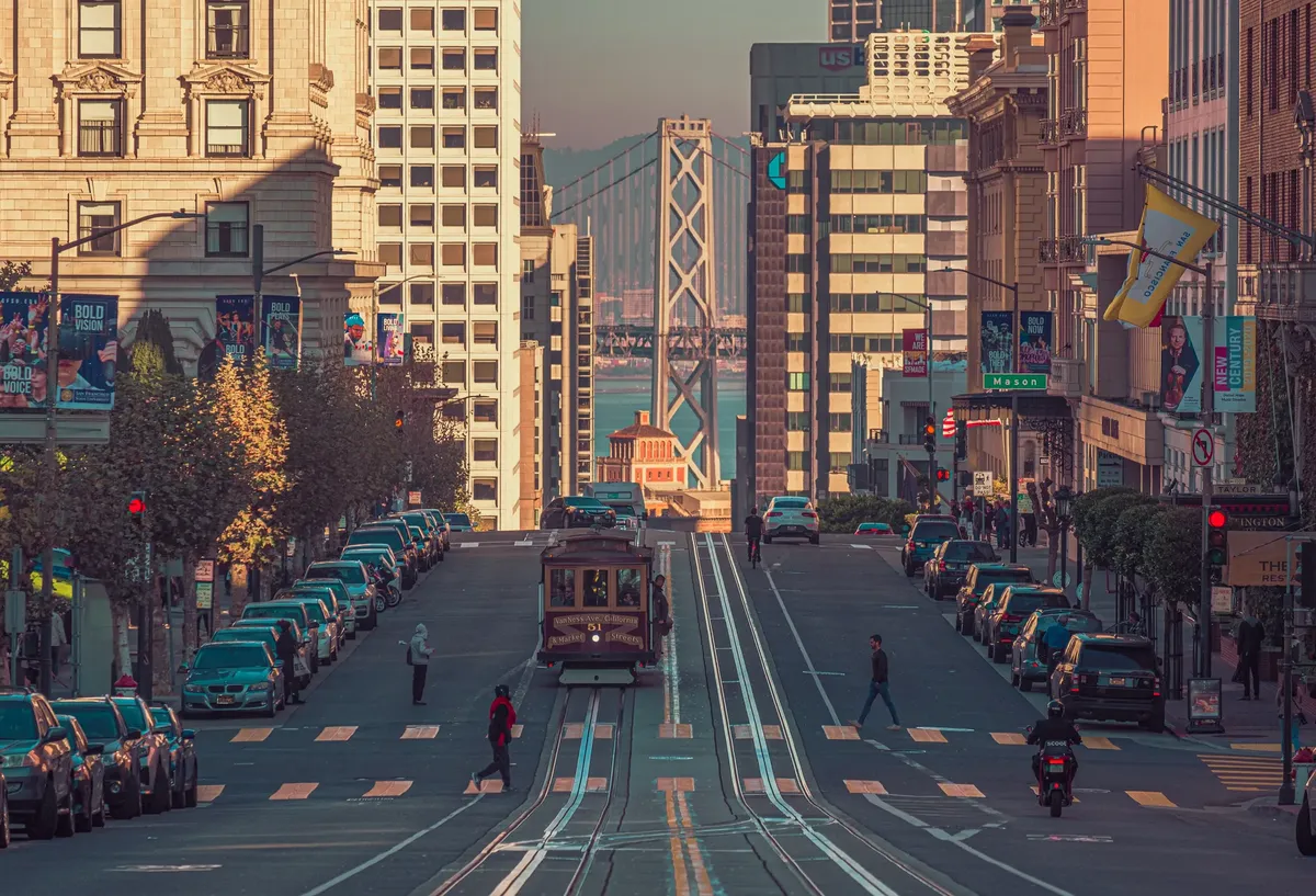 San Francisco street view featuring a classic cable car descending with city buildings and Bay Bridge in the background.