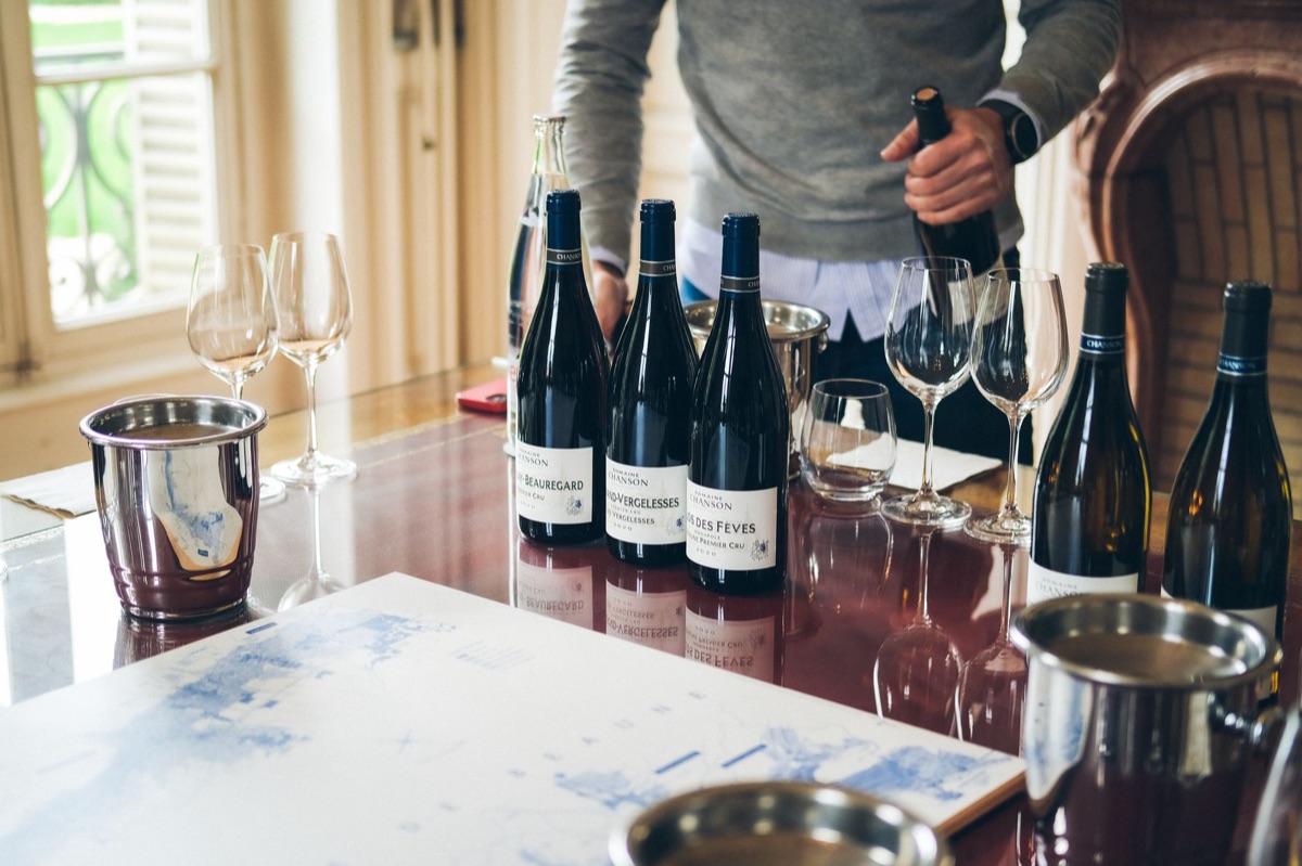 Un verre en verre rempli de vin rouge posé sur une table en bois, avec une bouteille de vin vintage à côté
