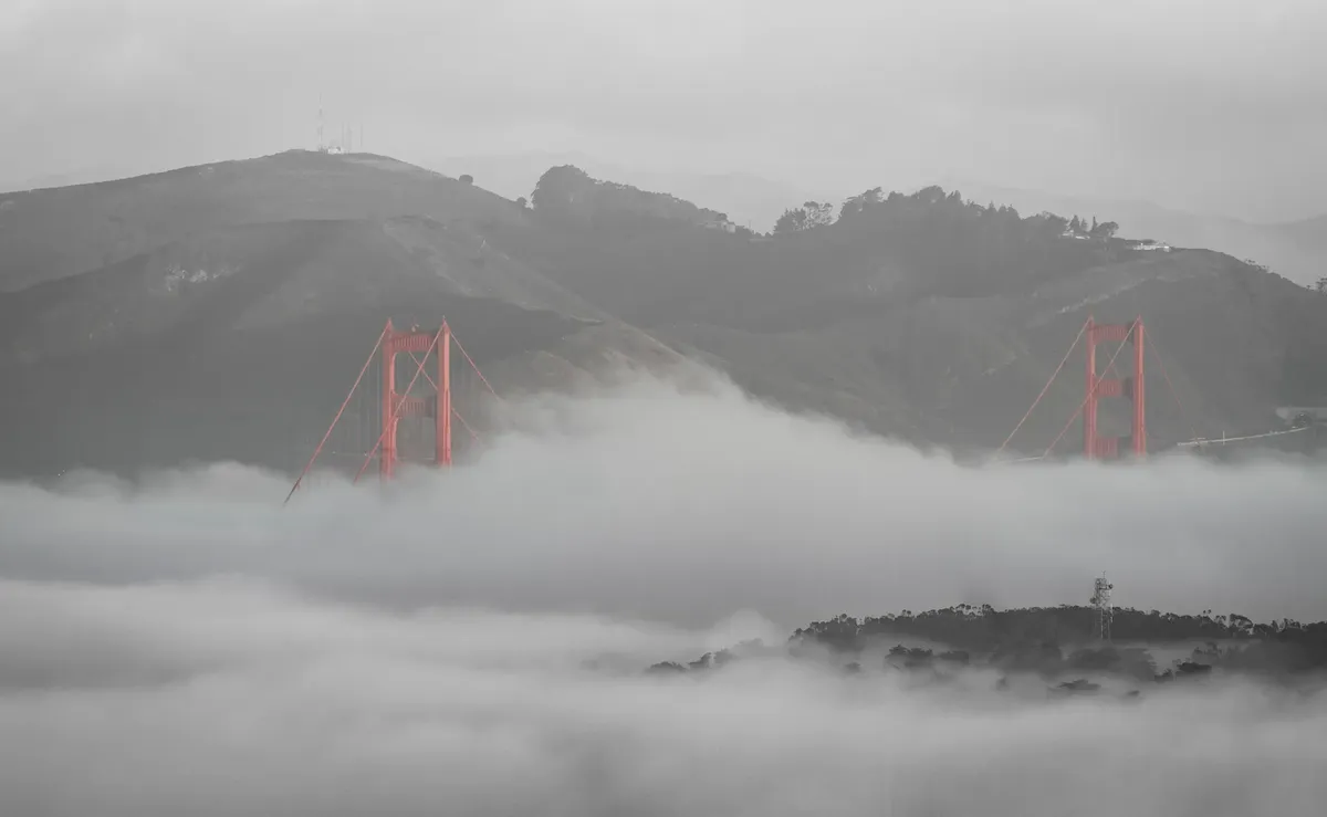 Golden Gate Bridge emerging from fog with hills in the background, capturing a moody San Francisco scene.